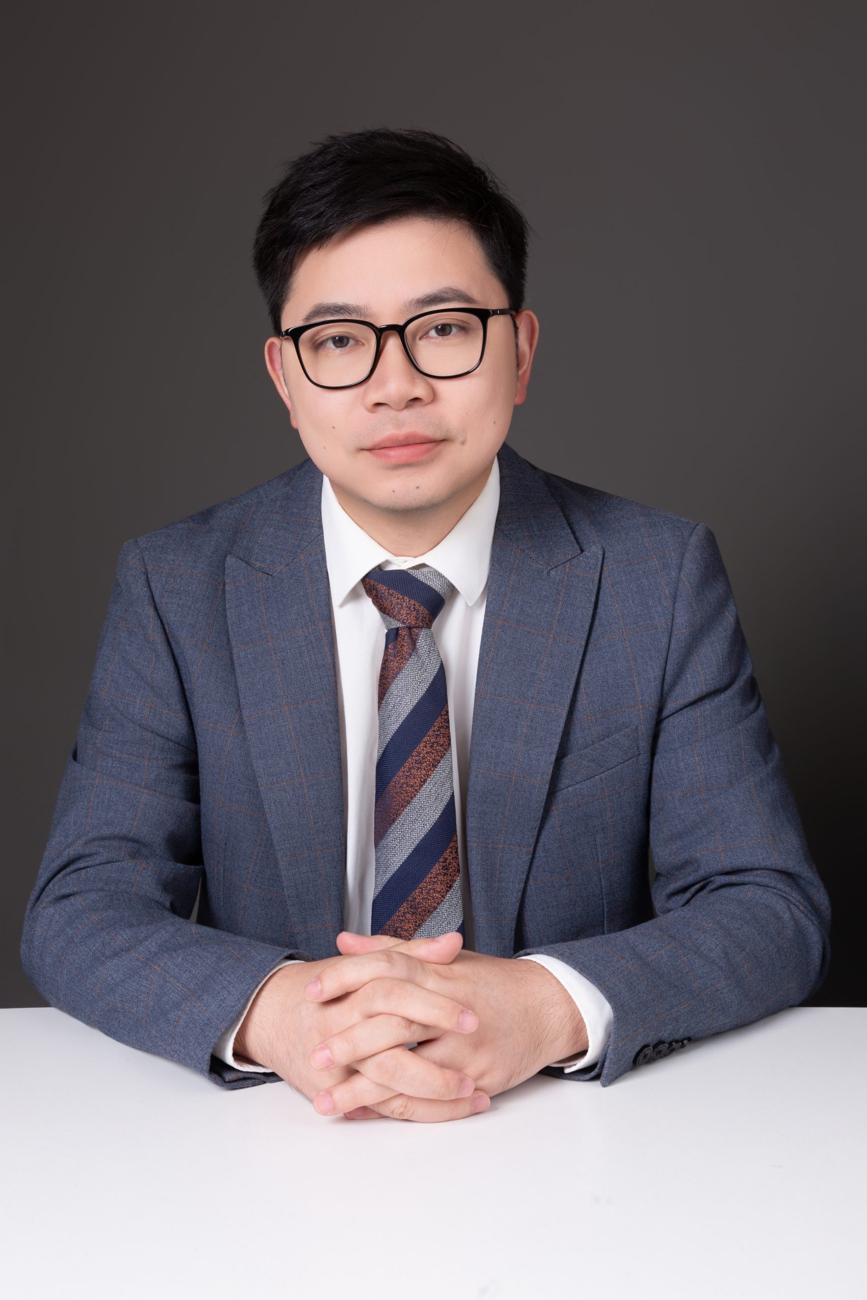Pascal 的形象照：灰色格纹西装，双手交叠